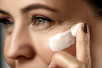 Yakın çekimde, bir kadın göz çevresine anti-aging kremi uyguluyor.