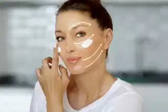 Genç bir kadın, yüzüne anti-aging kremi sürerken kamera karşısında gülümsüyor.