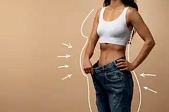 Beyaz üst ve büyük beden kot pantolon giymiş, fit bir kadın, bej arka plan önünde duruyor. Çizimle bel hattı ve incelme yönleri vurgulanmış.