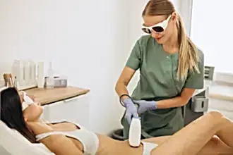 Gözlük takan bir estetisyen, bir kadının koluna buz lazer epilasyon tedavisi uyguluyor.