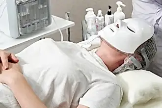 Bir kişi, beyaz bir LED maske takarak bir cilt bakımı tedavisi alıyor.