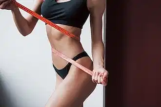 Siyah spor iç çamaşırı giymiş ve beline mezura dolamış fit bir kadın.